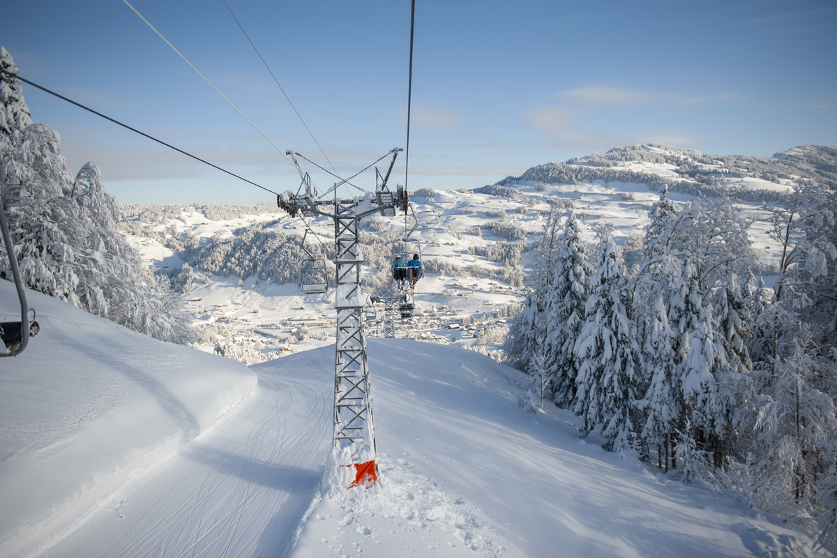 A picturesque view of Wolzenalp ski resort in Eastern Switzerland featuring a ski lift a skier enjoying the winter sports scene and a charming challet amidst the snow-covered landscape.