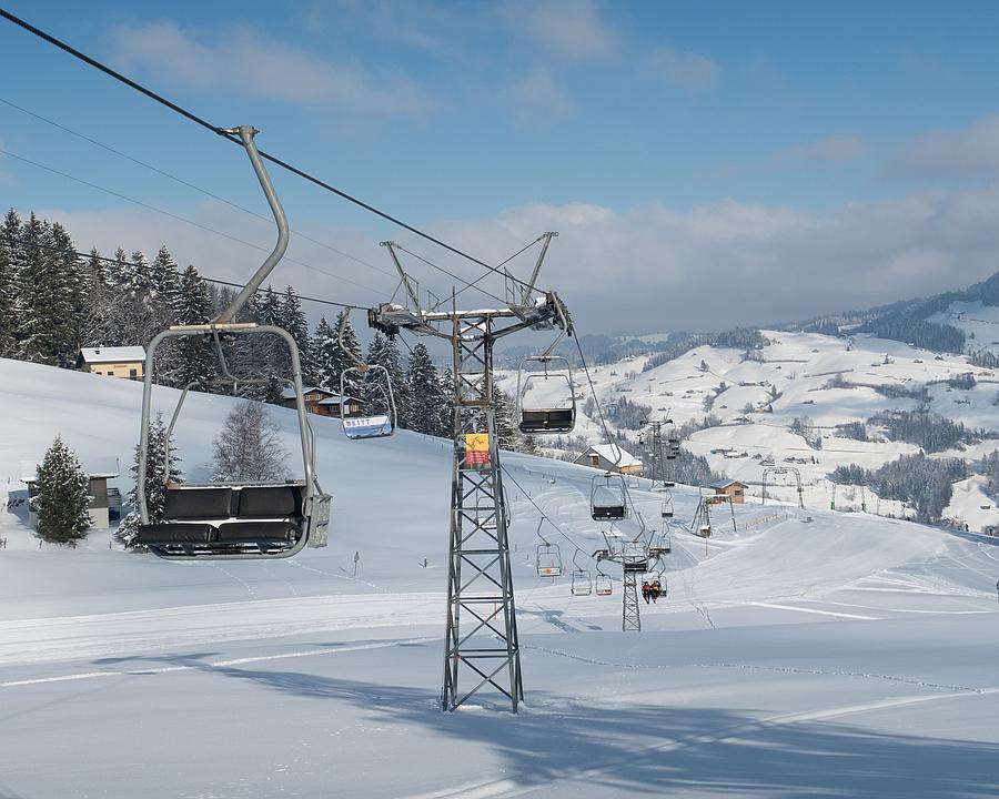 A ski lift ascending the snowy slopes of Wolzenalp in Eastern Switzerland with a quaint chalet and bustling winter sports scene visible in the background at the ski resort.