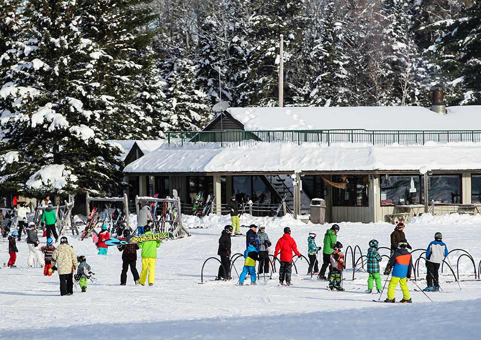 Winter scene at Searchmont Ontario showcasing an active ski resort with a chalet a ski lift and numerous visitors enjoying various winter sports.