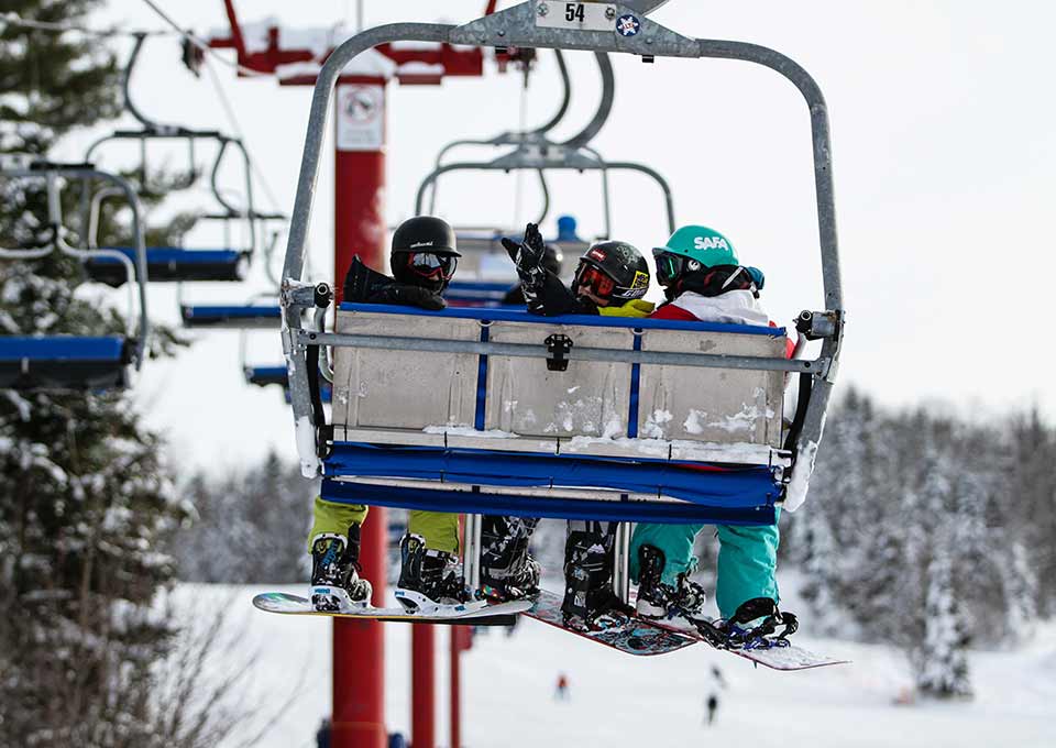 A ski lift in operation at Searchmont, Ontario, Canada, amidst a winter sports setting. Skiers and snowmobiles can be observed, enhancing the lively atmosphere of the ski resort.