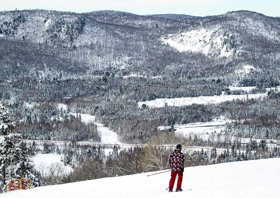 A skier is enjoying a day on the slopes at Searchmont Resort in Ontario Canada. The wintry scene includes a ski lift and a cozy chalet nestled among the pine trees.