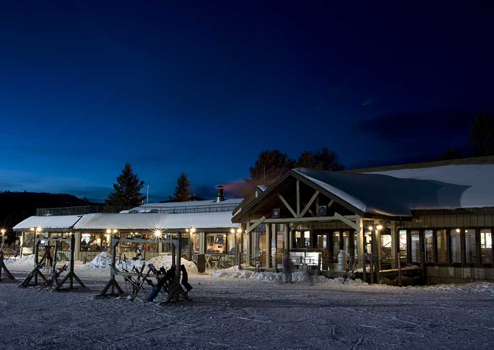 A lively winter scene at the ski resort in Searchmont, Ontario, Canada. Skiers and snowboards take to the slopes while others enjoy the comforts of the nearby lodge. Beautiful, snowy landscape surrounds the winter sports centre.