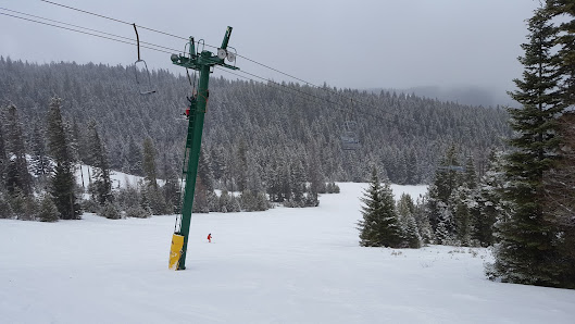 A ski lift ascends a snowy slope at Cooper Spur in Hood River Oregon. Skiers traverse the frosty landscape at this popular ski resort enjoying the winter sports scene. A snowmobile is slightly visible as well.