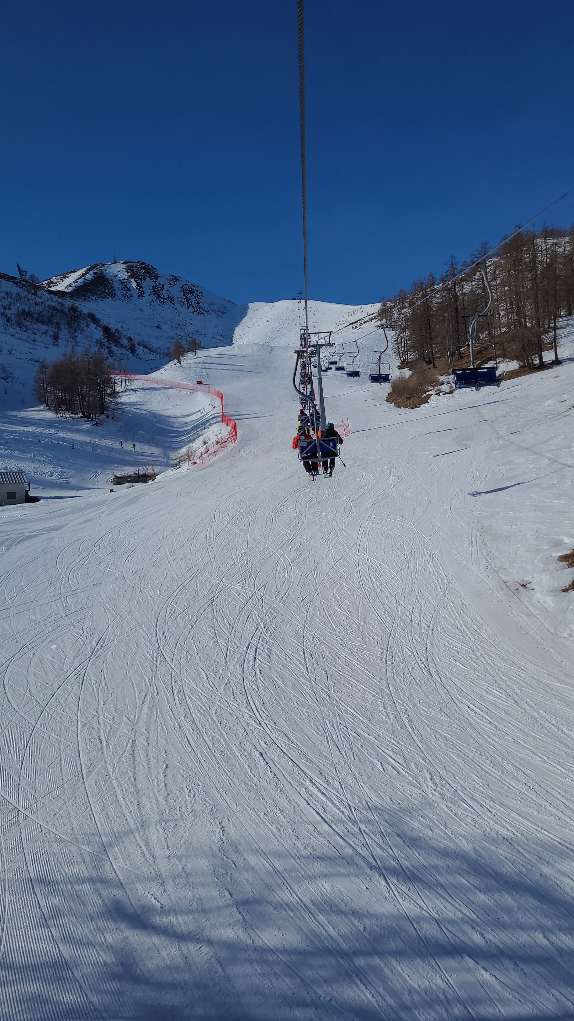 A skier traverses the snowy landscapes of Domobianca ski resort in Piedmont, Italy. A charming chalet and a ski lift are visible in the background, completing this winter sports scene.