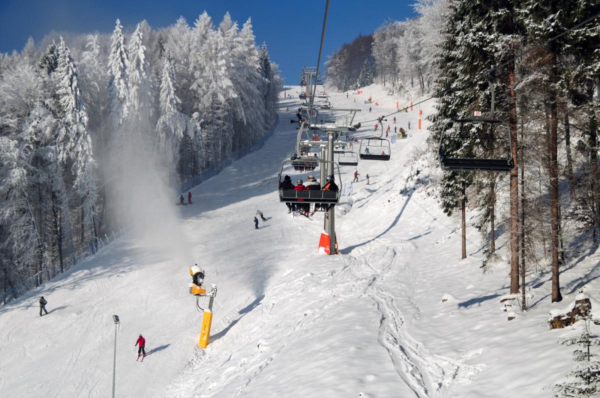 Winter scene at Dwie Doliny ski resort in Szczawnik, Poland showcasing a ski lift, skiers enjoying the slops amidst stunning snowy scenery, and a charming chalet in the distance.