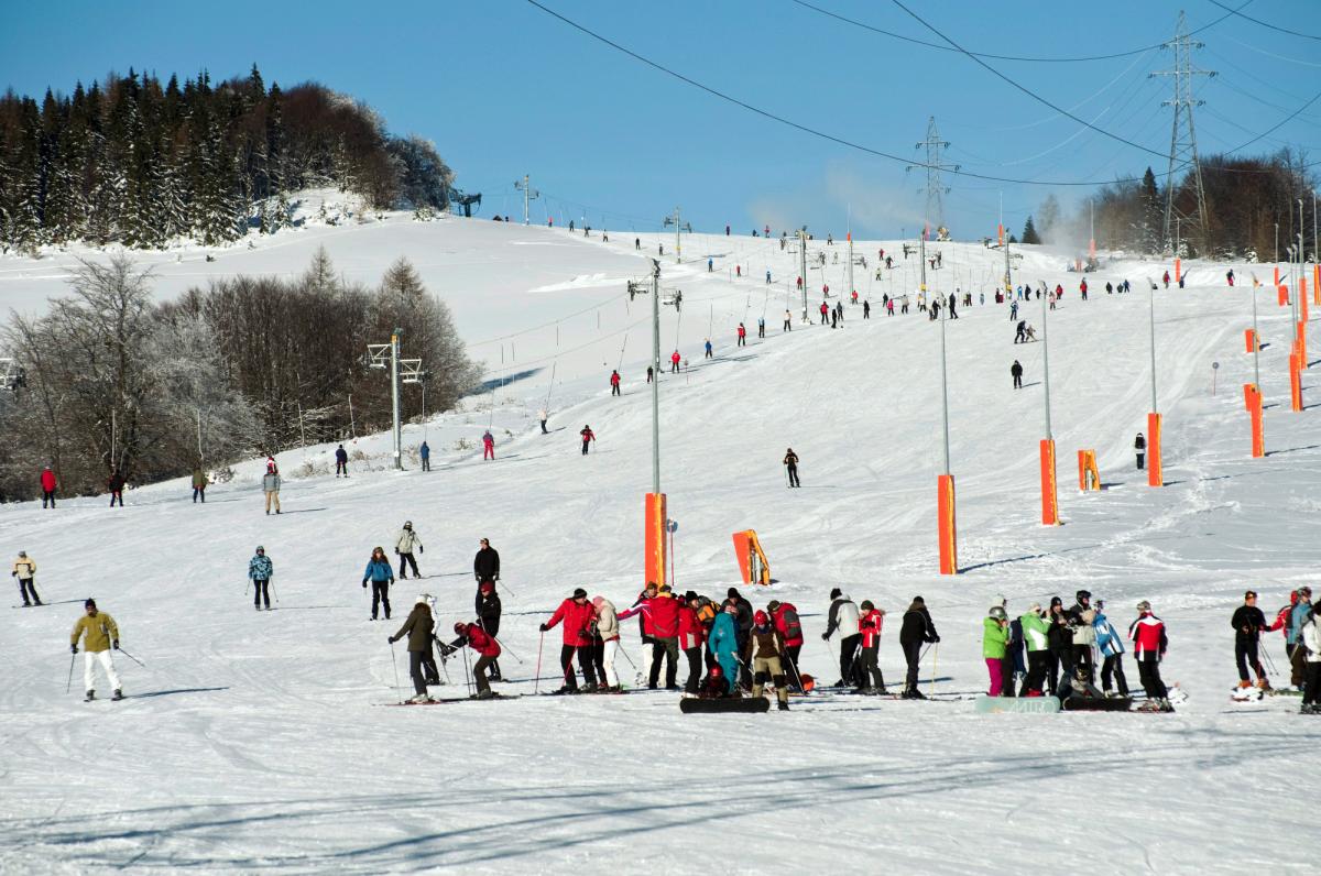 Winter scene at Dwie Doliny - Szczawnik I chairlift in Wierchomla Mała, Poland, featuring a bustling ski resort, a charming chalet, and busy ski lifts.