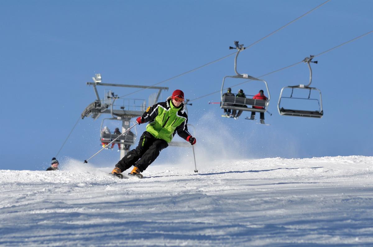 A skier enjoying a winter day on the slopes at Dwie Doliny ski resort in Poland, with a ski lift and a snowmobile visible in the background.