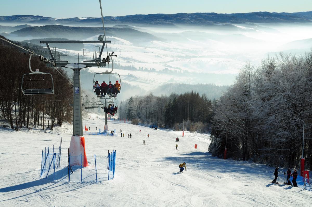 Winter scene at Dwie Doliny ski resort in Poland, featuring a ski lift transporting skiers amidst snow-capped mountains, with a chalet in the background.