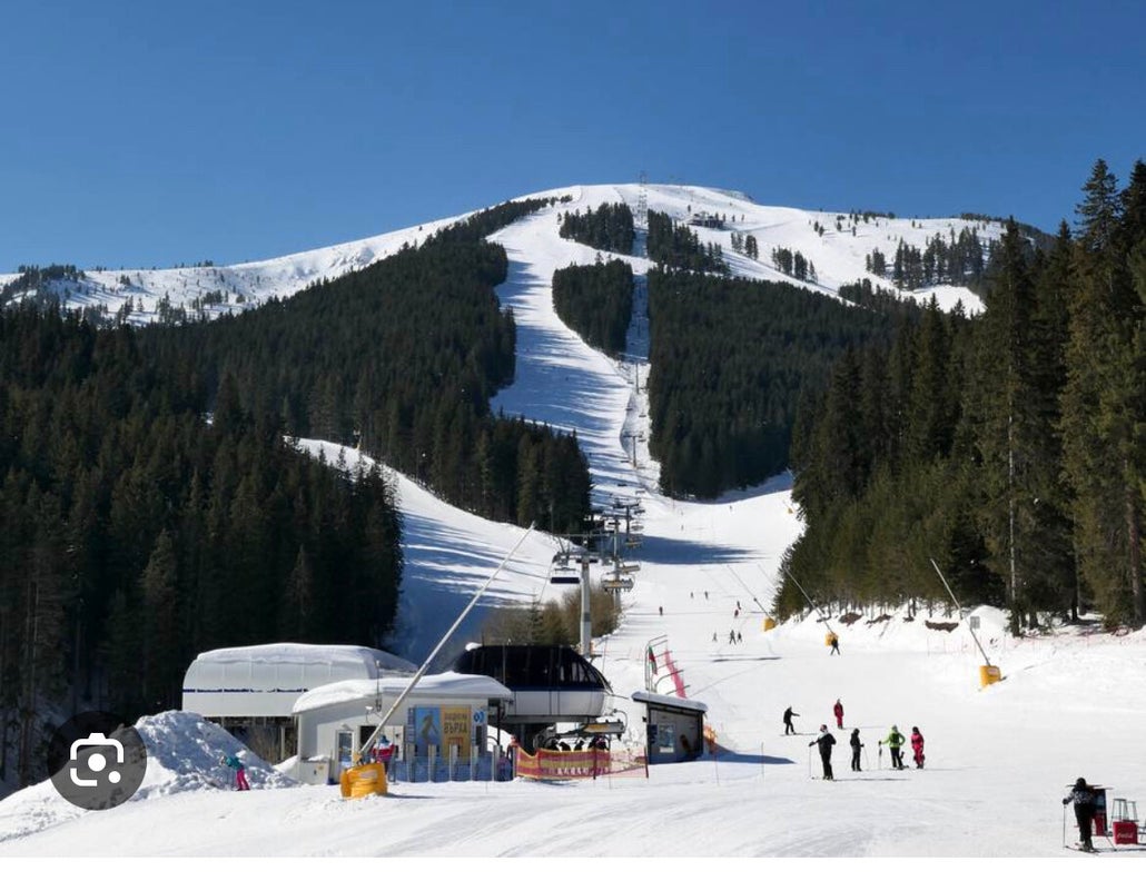 Ski resort in Bansko, Bulgaria featuring snow-covered slopes bustling with winter sports enthusiasts, with a charming challet in the backdrop.