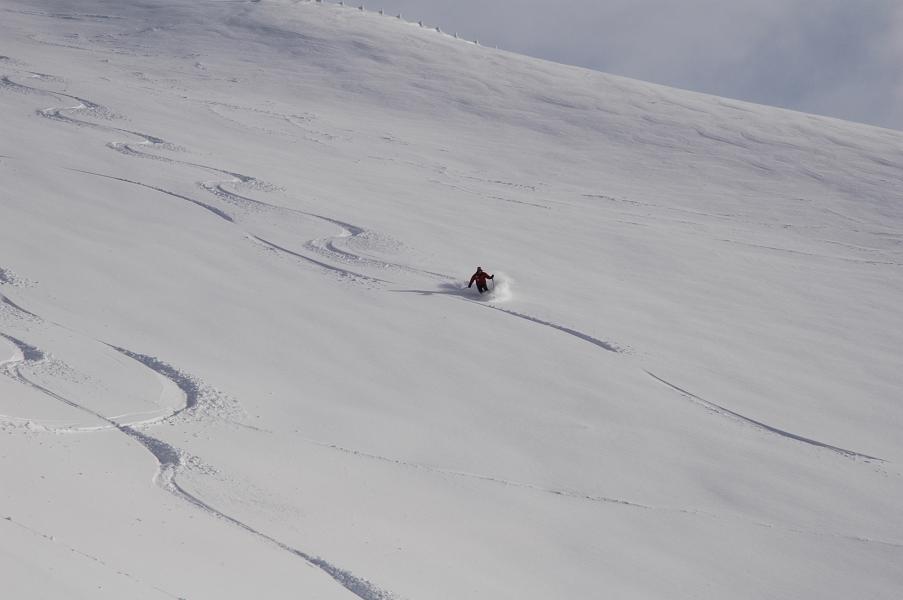 A skier gliding down snowy slopes in Monte Terminillo, Italy, against the backdrop of a rustic chalet. Winter sports activities underway in the serene mountainous landscape.