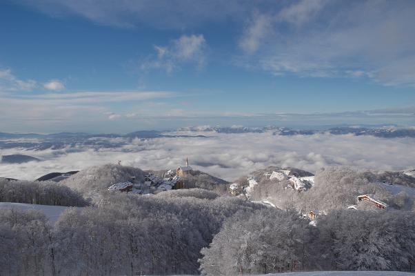 Winter scene at Monte Terminillo in Rieti, Italy, featuring a charming chalet amidst snow-clad landscape with faint outline of a mountain in the backdrop.