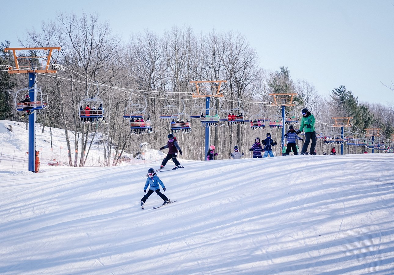 A vibrant winter sports scene at Mont Rigaud in Quebec, Canada, showcasing lively skiers enjoying their runs, amidst picturesque snow-covered slopes.