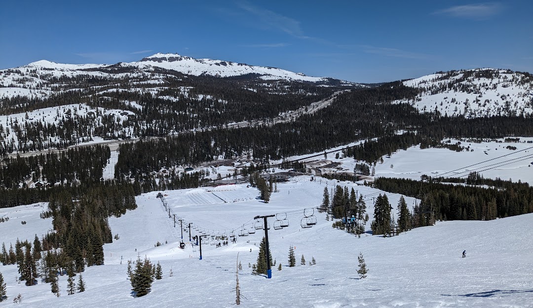Ski resort in Soda Springs, Lake Tahoe showcases bustling winter sports scene with a ski lift leading up to snow-covered slopes, with a skier prepping for the joyful slide downhill.