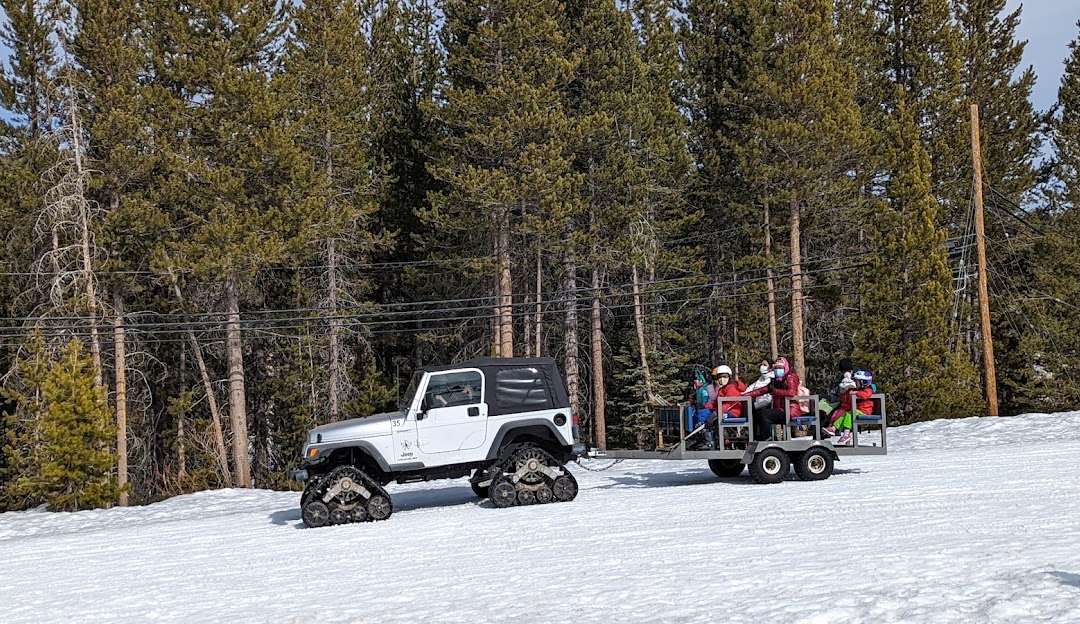 A snowmobile dominates the winter sports scene at Soda Springs in Lake Tahoe California with a ski lift and ski resort subtly visible in the background. A family can be spotted enjoying skiing.