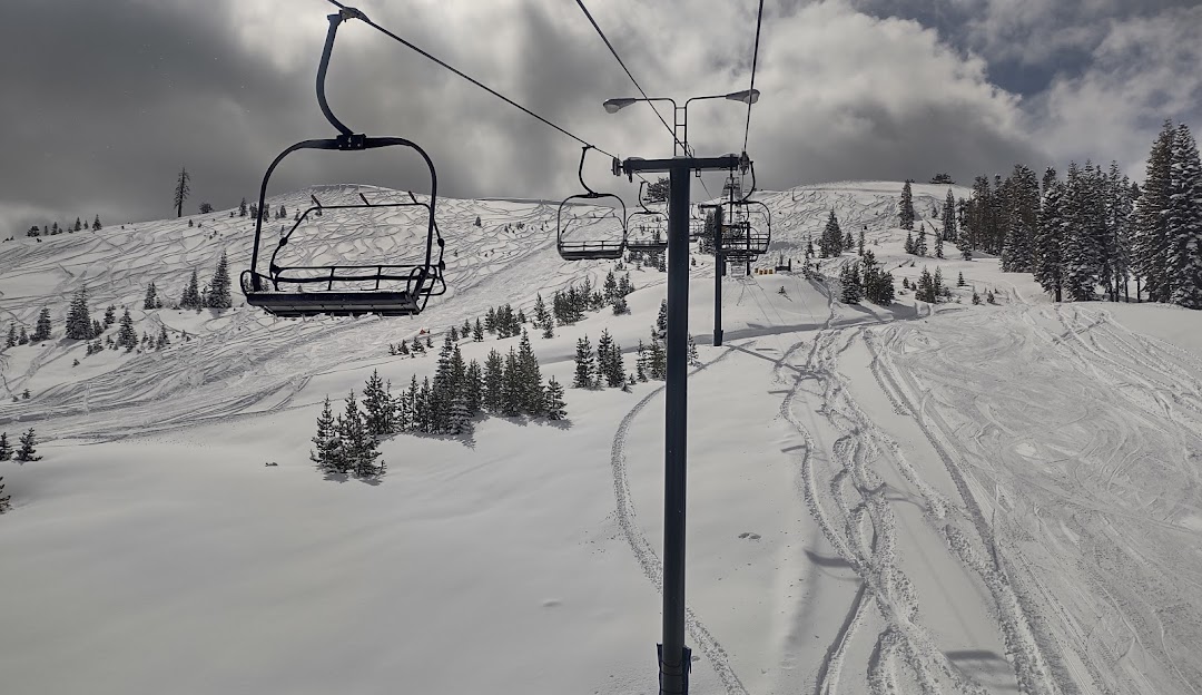 Ski lift ascending snow-covered slopes in Soda Springs, Lake Tahoe, at a ski resort, highlighting a vibrant winter sports scene. A chalet is spotted in the distance.