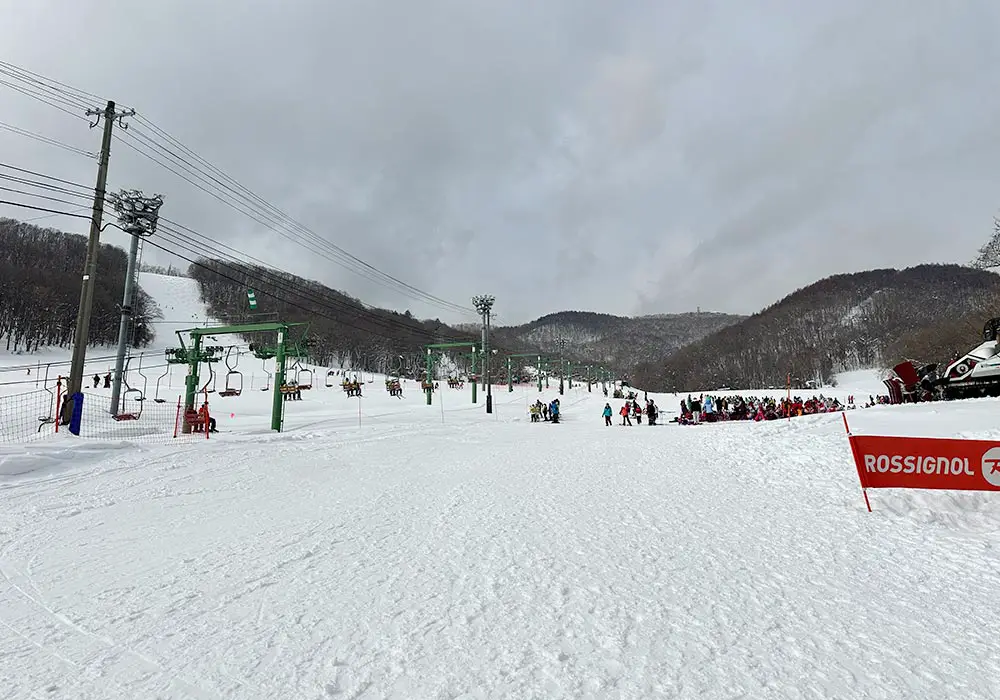 A picturesque winter scene at Moiwayama Ski Jominamishamen in Japan, capturing a bustling ski resort complete with skiers enjoying the slopes, a ski lift in operation, and stunning snow-covered scenery.