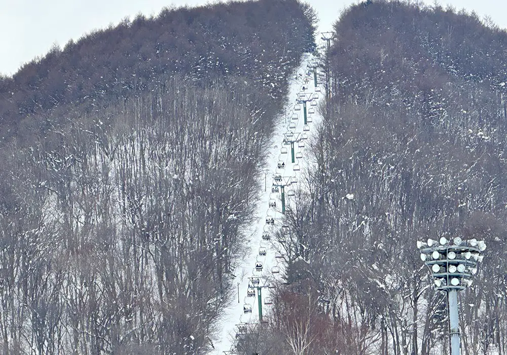 A skier is enjoying a fun day at the Moiwayama Ski Jominamishamen in Kitanosawa, Hokkaido, Japan, with snow-covered slopes and a ski lift in the backdrop, offering a picturesque winter sports scene at the ski resort.