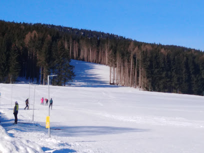 Winter sports scene at Ož – Orlické Záhoří in Czech Republic, featuring a ski resort with busy slopes, a winter sports centre, a welcoming challet and a ski lift.