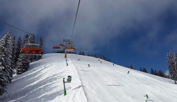 A skier enjoying a run on the snow-covered slopes of a ski resort in Ož – Orlické Záhoří, Czech Republic, with a ski lift in the background.