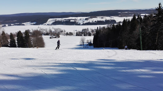 A skier enjoying a winter sports scene at Ož – Orlické Záhoří in the Czech Republic with a chalet and other resort facilities in the background.