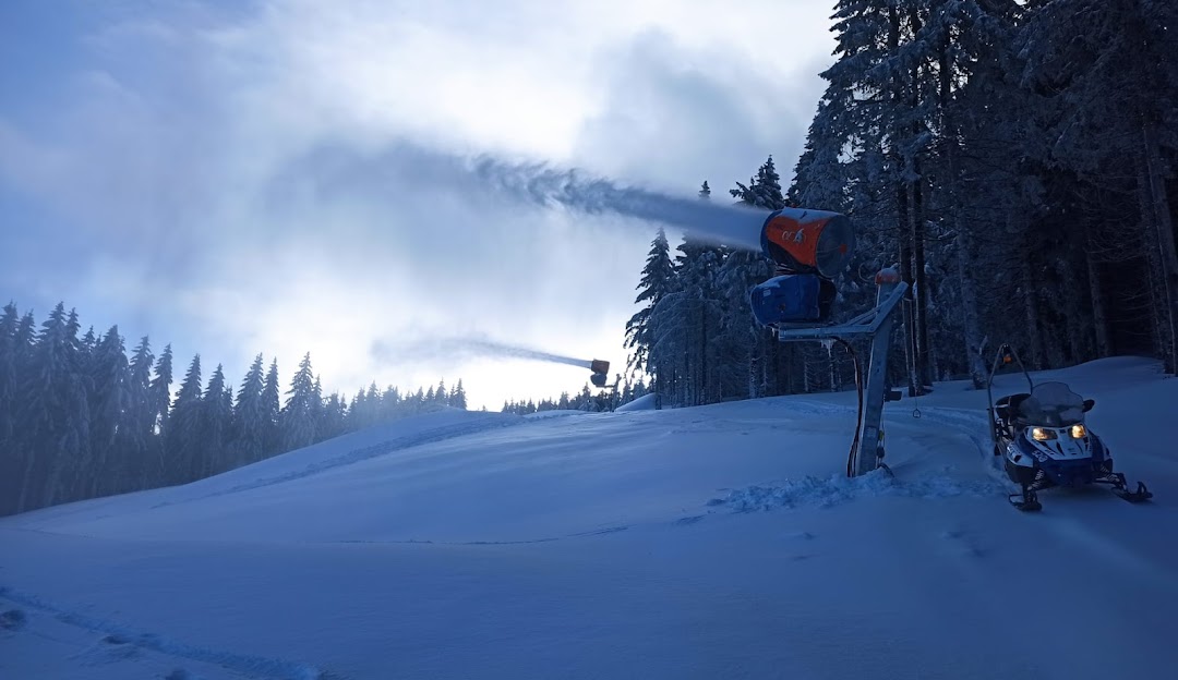 A skier descending a slope in Orlické Záhoří Czech Republic with a ski lift and other elements of a winter sports scene like a snowmobile in the backdrop.