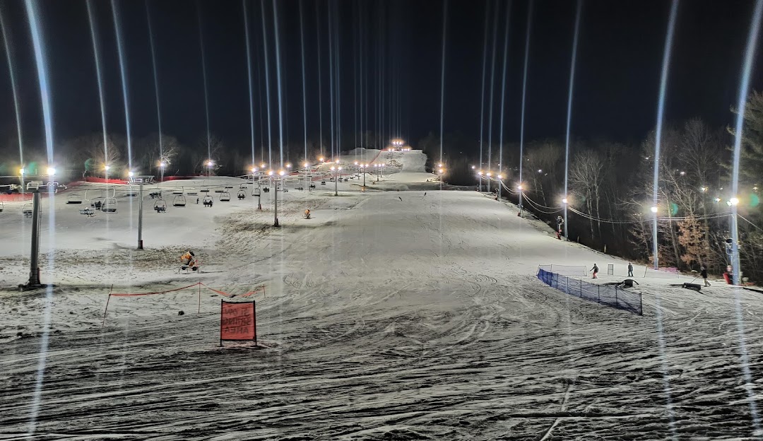 Winter scene at West Mountain in The Adirondacks, Queensbury, NY, featuring bustling ski resort activities including a ski lift transporting skiers uphill.