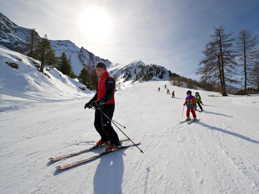 Winter sports scene at Cogne - Gran Paradiso in Italy with a family skiing down the slopes, a solitary skier nearby and a quaint chalet nestled amidst the ski resort.