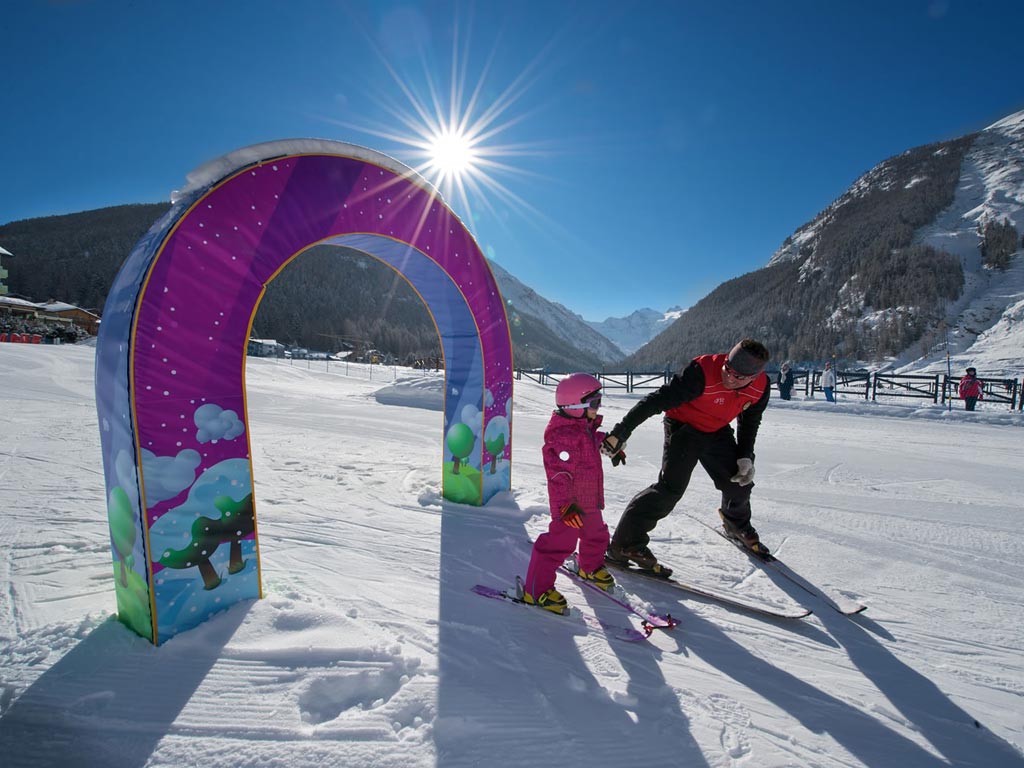 A vibrant winter sports scene in Cogne - Gran Paradiso Italy featuring a bustling ski resort with a skier and a family enjoying skiing.