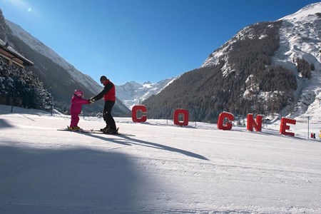 A winter scene at the Cogne – Gran Paradiso ski resort in Italy showcasing a bustling winter sports center filled with skiers including a family enjoying their time on the expansive snowy slopes.