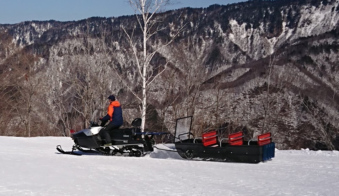 A snowmobile rests in a stunning winter landscape at Honokidaira in Takayama, Japan. A chalet and ski resort are faintly visible in the background, creating a picturesque winter sports scene.