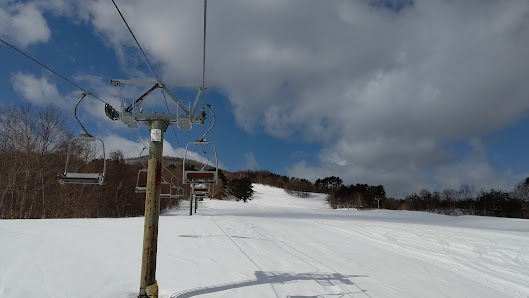 Ski lift ascending over a snowy winter landscape in Hiraniwa Kogen, Japan. Skiers enjoy the slopes beneath, nearby a cozy chalet. The atmosphere conveys a typical ski resort scene.
