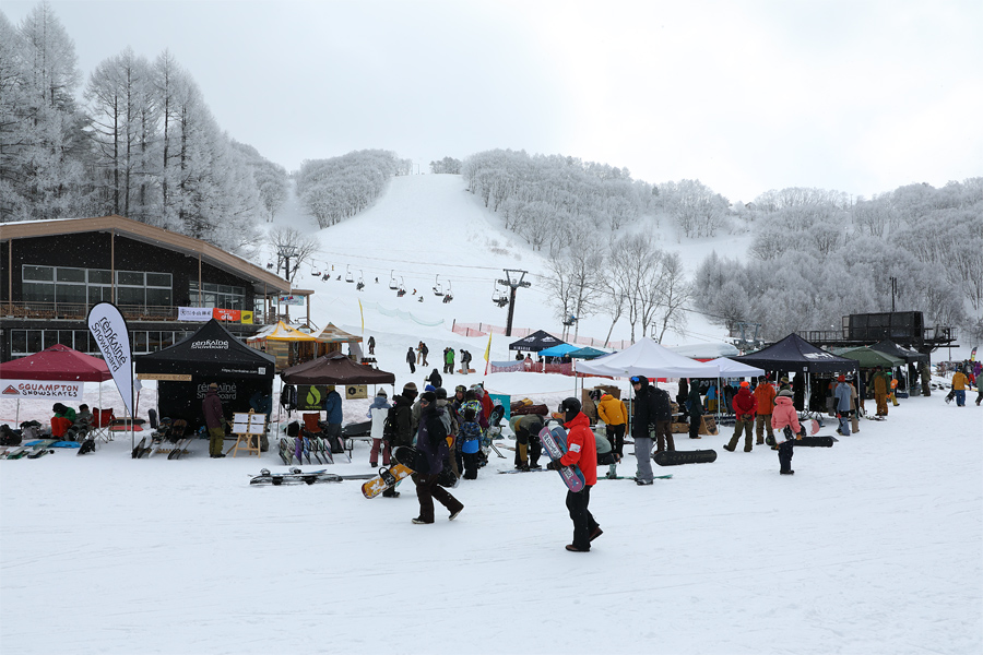 Winter scene at Rewild Ninja Snow Highland in Japan, featuring skiers enjoying the pristine snowy slopes, framed by beautiful winter-touched trees, with a cosy chalet nestled in the background.
