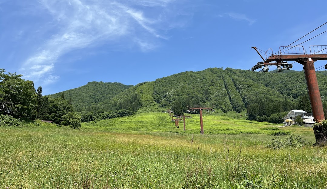Ski lift ascending a sunlit mountain at the Star Spur Ryokufu Resort in Japan, with a chalet nestled nearby and a skier enjoying the clear day.
