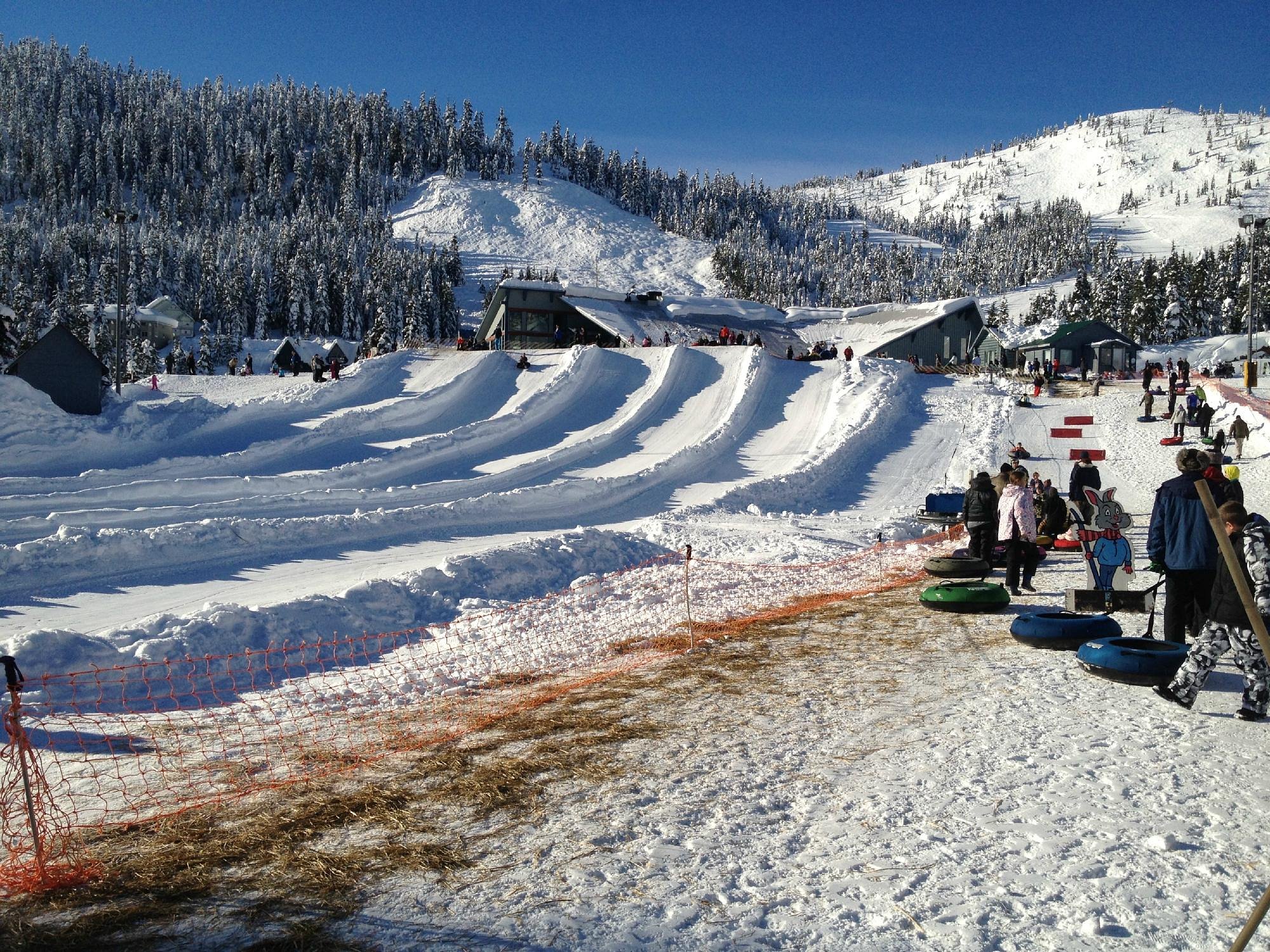 Winter sports enthusiasts enjoy a day at Sasquatch Mountain Ski Resort in Hemlock Valley, Agassiz, British Columbia, featuring snow-covered slopes and a snowmobile in the distance.