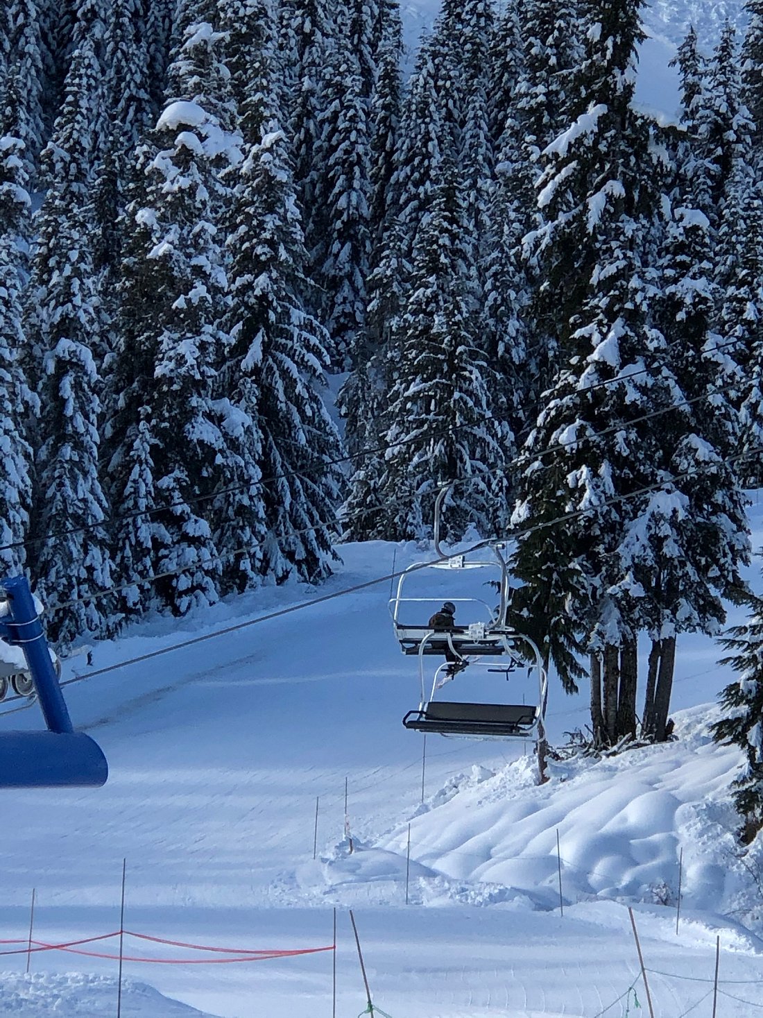 Winter sports enthusiasts enjoying Sasquatch Mountain ski resort in Hemlock Valley, Canada, visible are a ski lift in operation and a snowmobile, all amidst a snowy landscape.