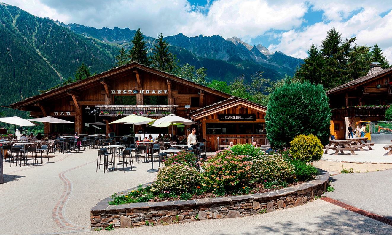 Les Planards in France - a restaurant with tables and umbrellas in front of mountains.