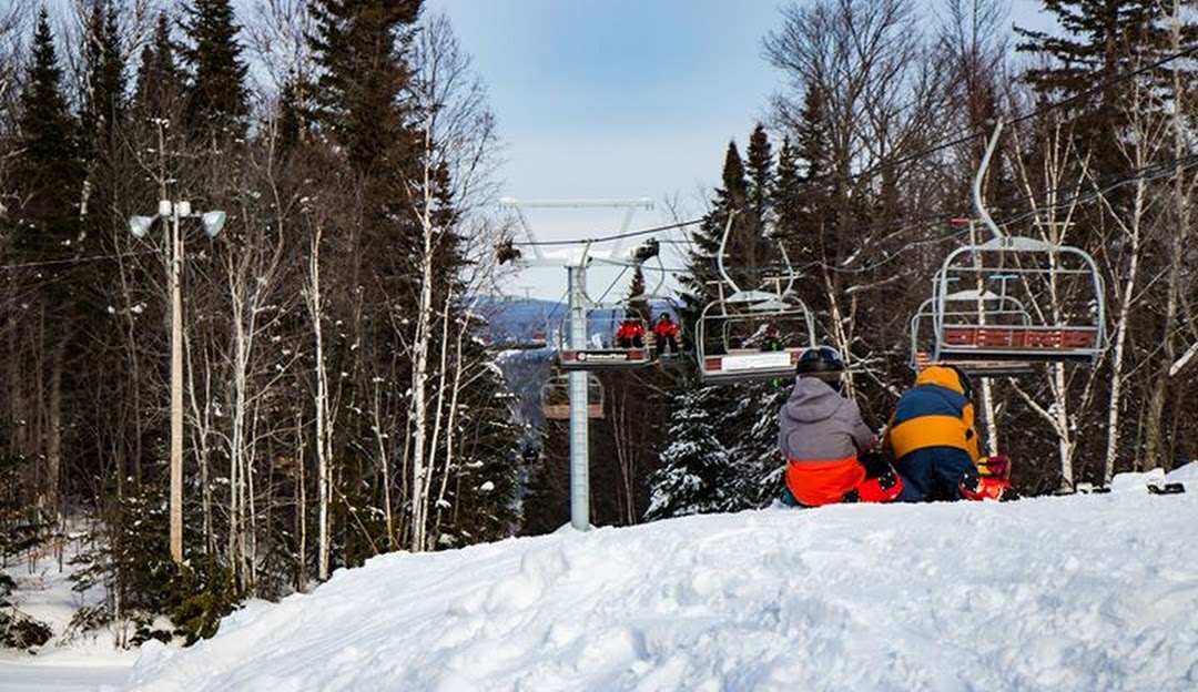 Ski lift ascending at the Mont Farlagne ski resort in New Brunswick, Canada, dotted with winter sports enthusiasts enjoying their ski session.