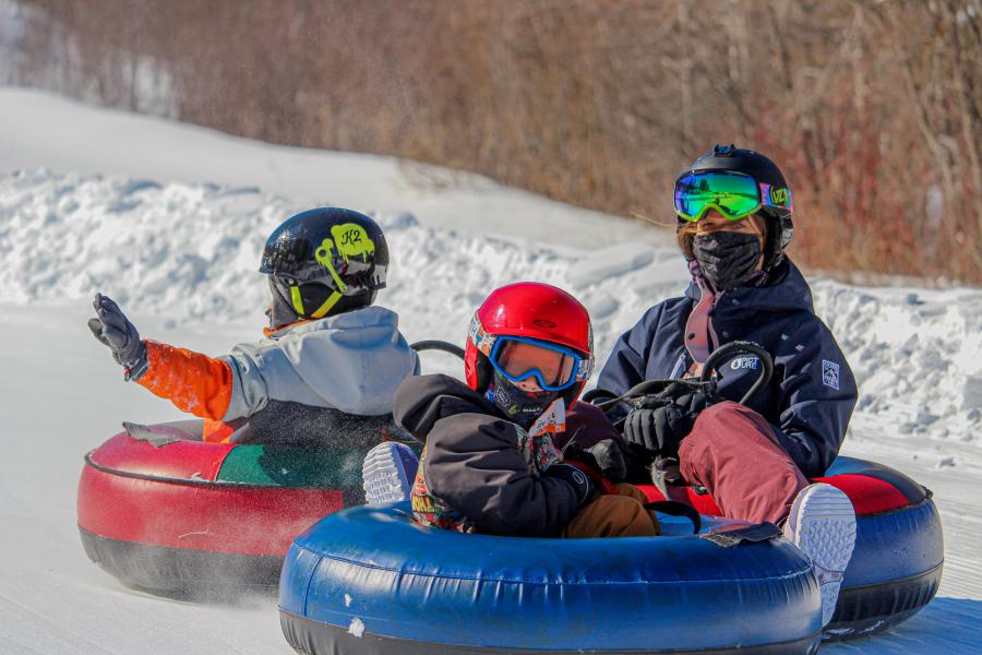 Winter sports scene at Mont Farlagne in Saint-Jacques, New Brunswick, Canada, featuring a family and a group of people skiing at the resort, with a snowmobile on the side.