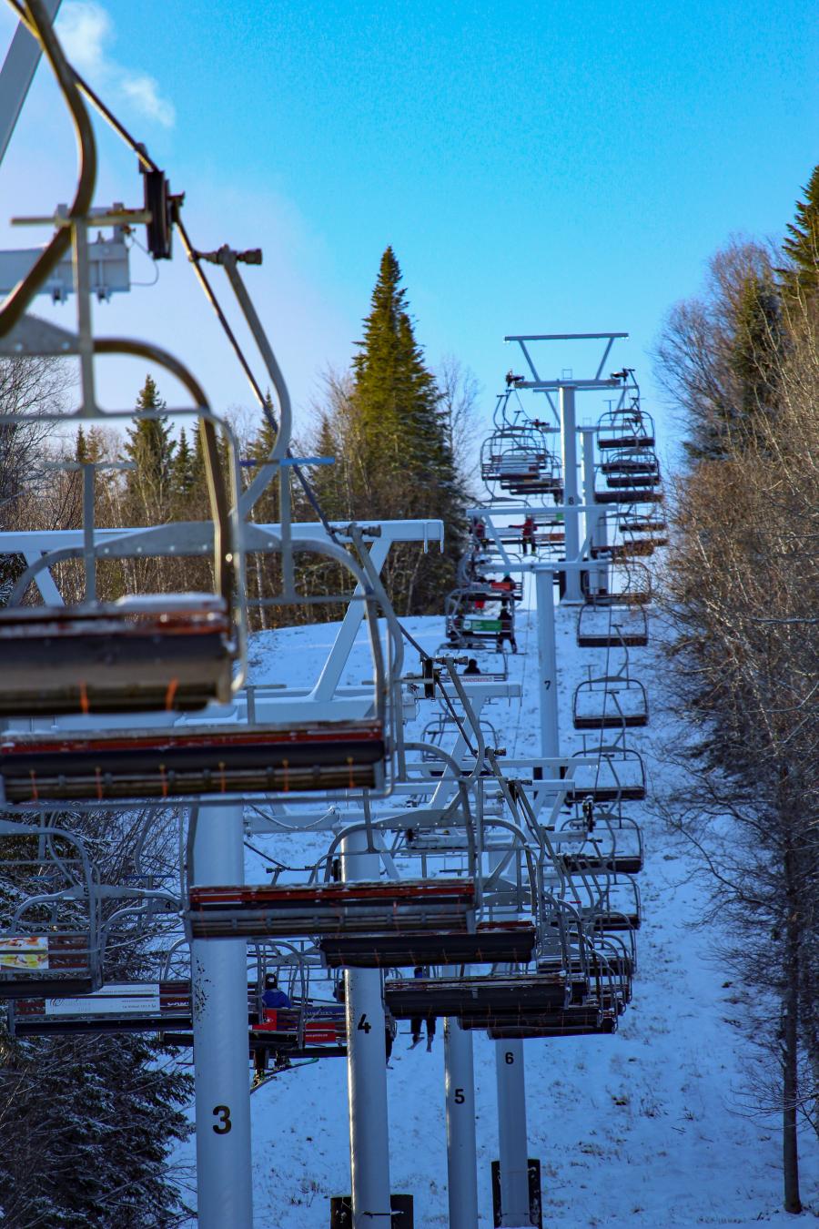 A vibrant winter sports scene at Mont Farlagne ski resort in New Brunswick Canada featuring a ski lift ascending the snowy mountainside.