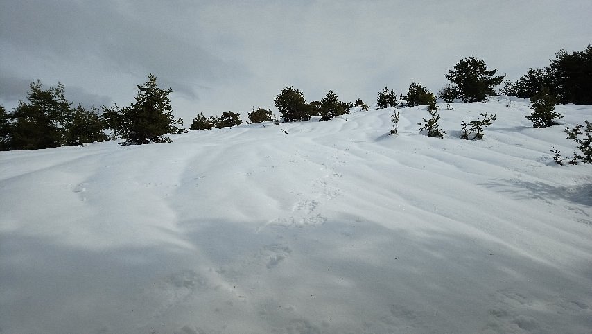 Winter scene at Gréolières Les Neiges in France, featuring a charming chalet nestled against a snow-covered mountain backdrop. Activity bustles with winter sports and a snowmobile presence.