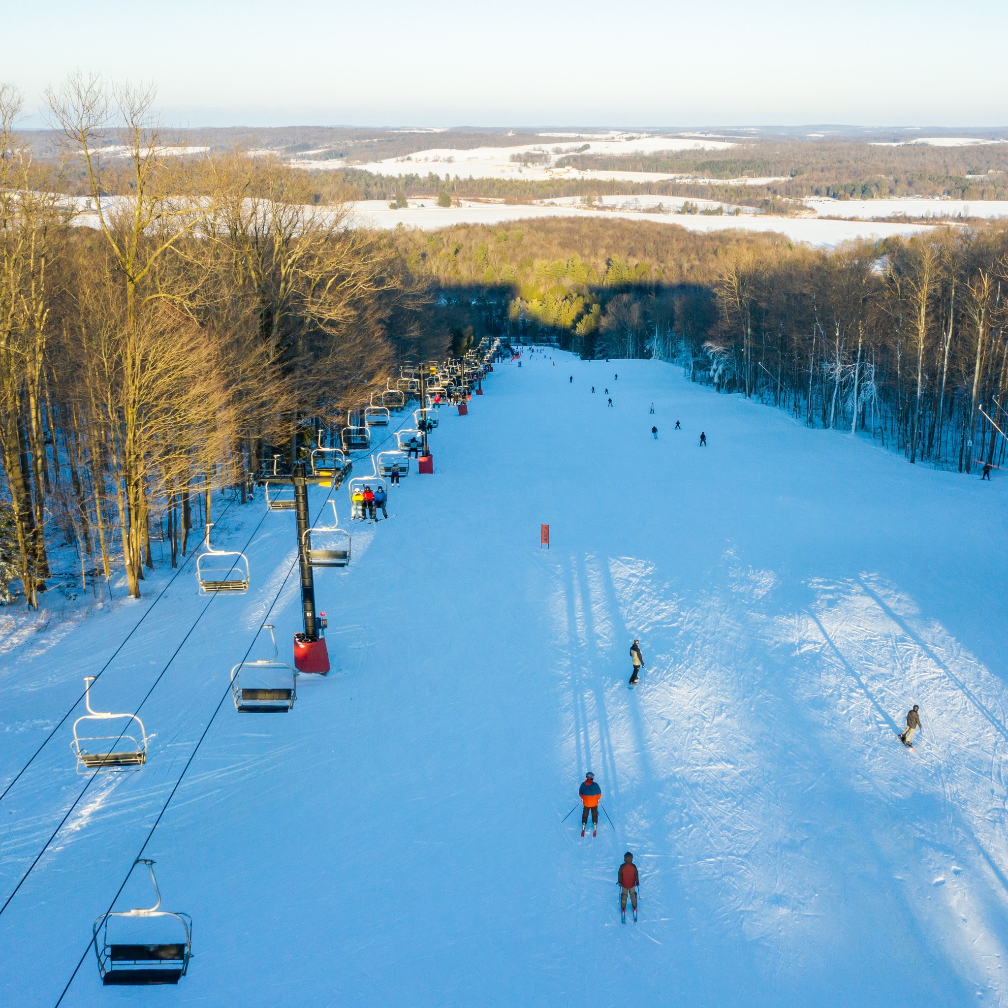Winter sports enthusiasts enjoying a day at Peek n Peak ski resort in Clymer, New York, with a scenic view of snow-covered slopes, a ski lift and a bustling winter sports centre.