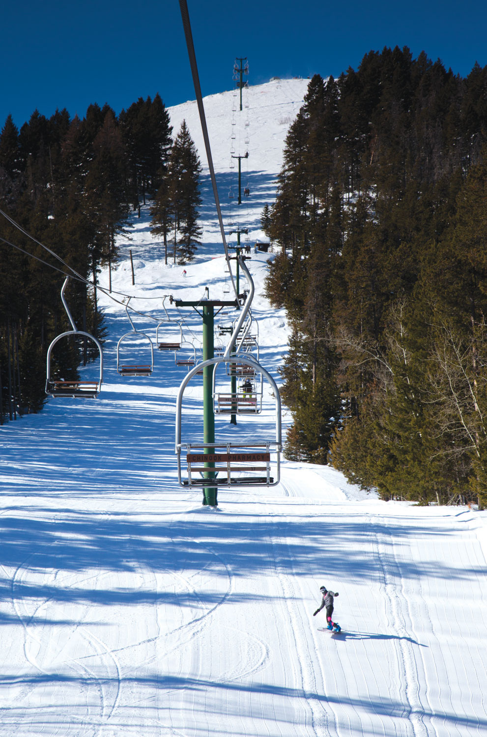 A picturesque view of Bear Paw Ski Bowl in Montana showcasing a ski lift in the foreground with a skier enjoying the snowy slopes in a vibrant winter sports scene.