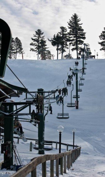 View of Pine Mountain ski resort in Iron Mountain Michigan featuring a ski lift traversing the snow-covered slope and a chalet nestled amidst a wintery landscape.