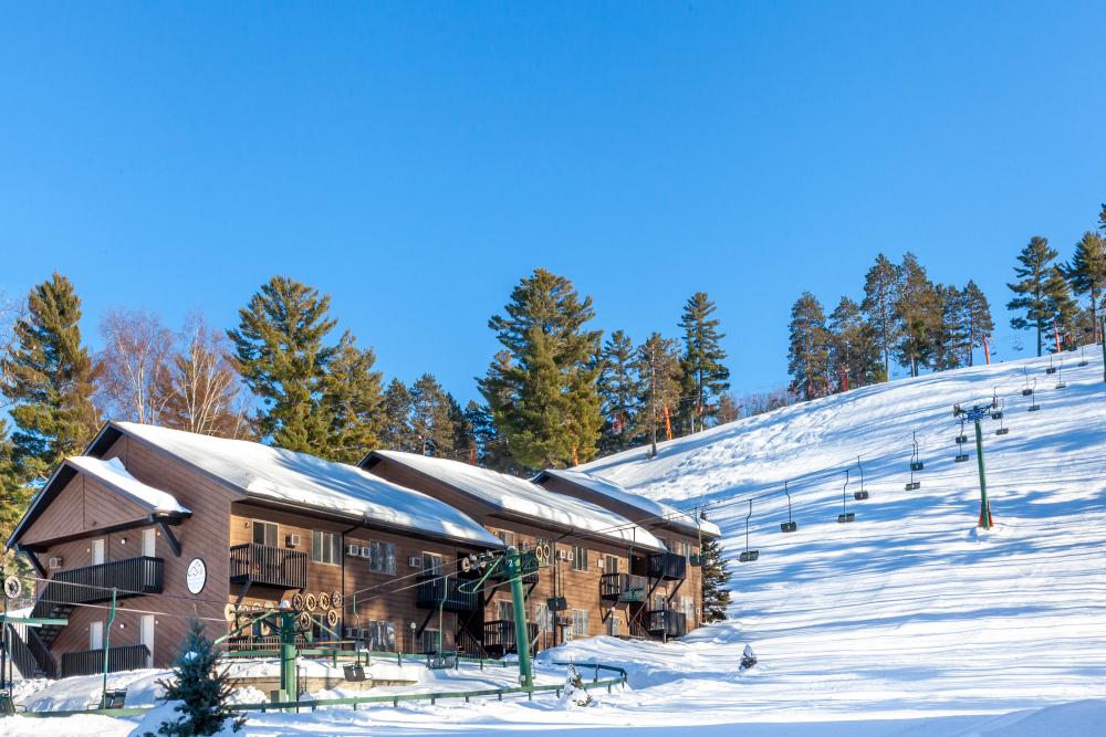Ski resort at Pine Mountain, Iron Mountain, Michigan during winter season, with a bustling winter sports scene at a lodge and winter sports centre amidst a stunning snow-filled landscape.