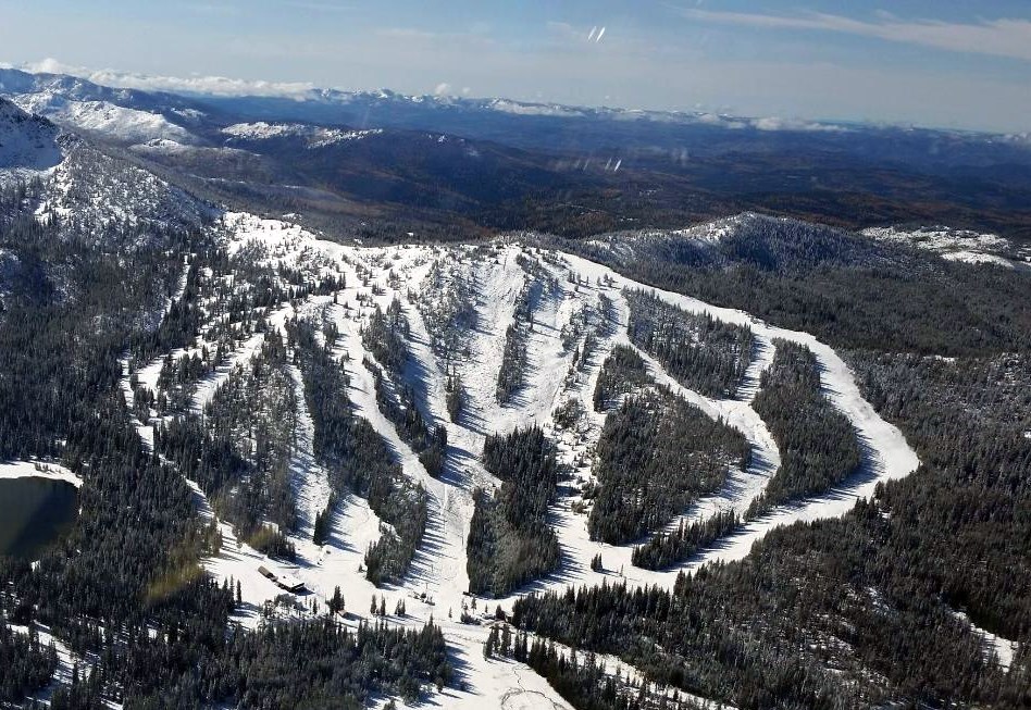 Ski goers enjoying a sunny day at Anthony Lakes Mountain Resort in North Powder, Oregon. The snow-covered slopes of the mountain are sprinkled with skiers and a ski lift is visible, transporting visitors further up.