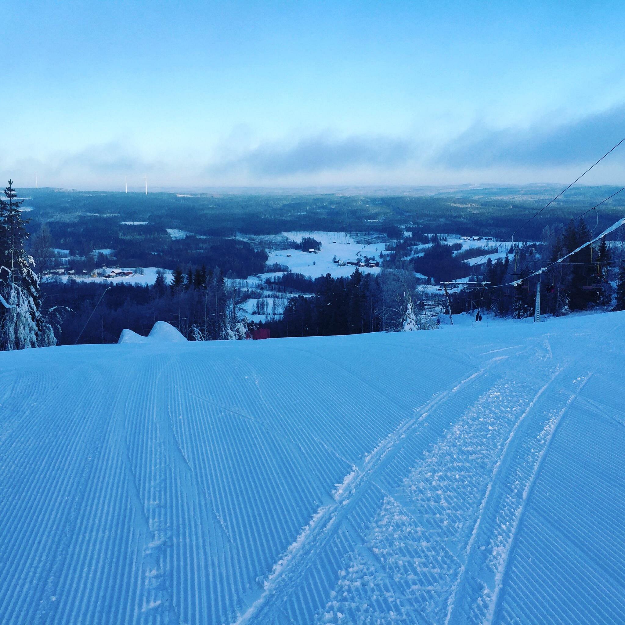 Winter sports scene at Kungsberget, Järbo, Sweden with a ski resort, including a chalet and a ski lift. A skier is also visible.