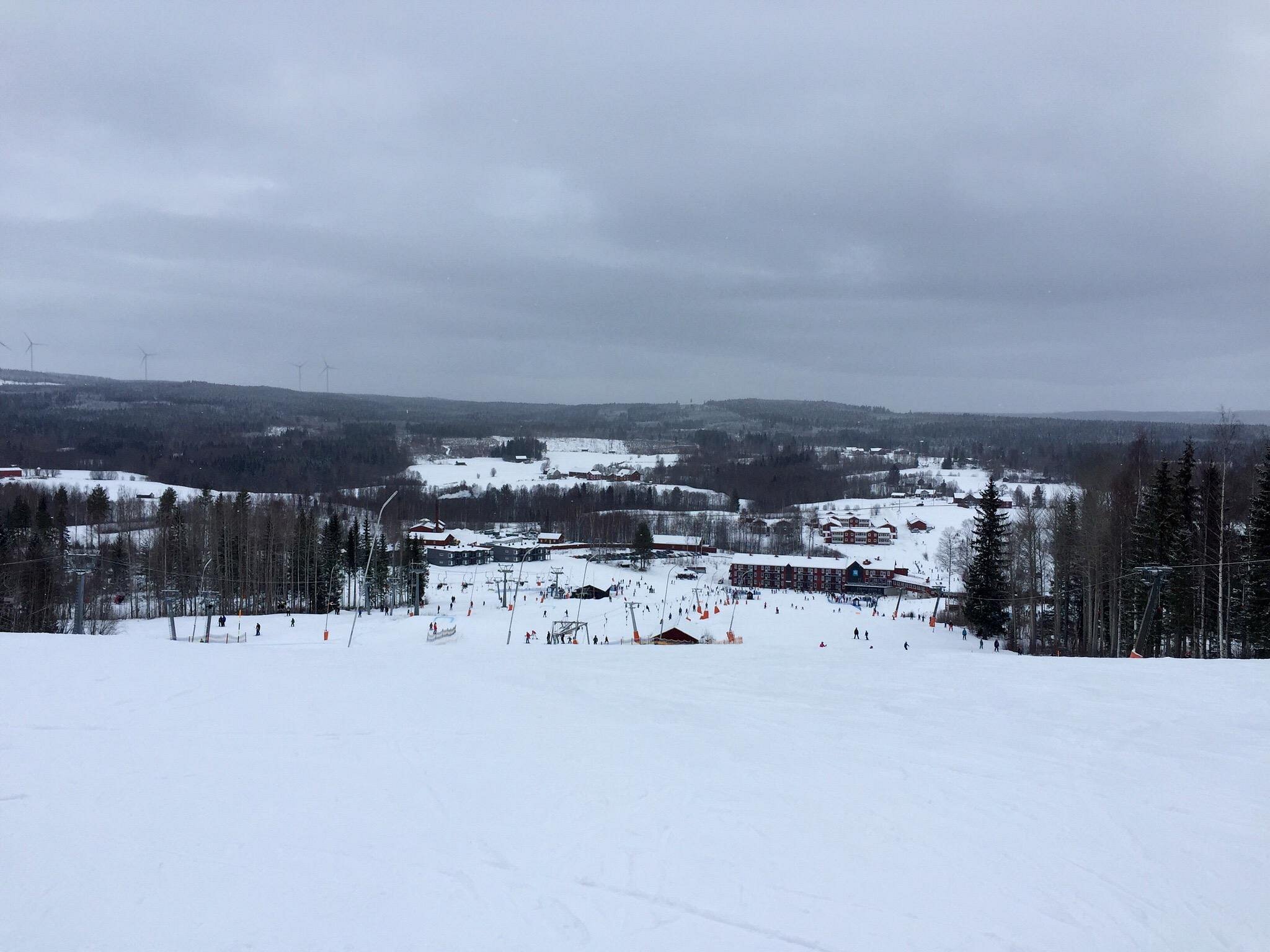 Winter scene at Kungsberget resort in Järbo, Sweden, showcasing snow-covered slopes, active skiers descending the hill, and a ski lift carrying more adventurers to the top.
