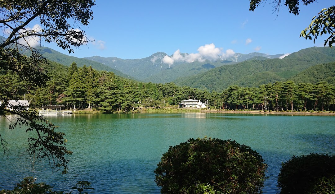 Sunny day at Shirakabako Royal Hill, Japan, featuring a serene lake, a charming challet amidst stunning winter scenery, and mountains in the backdrop.