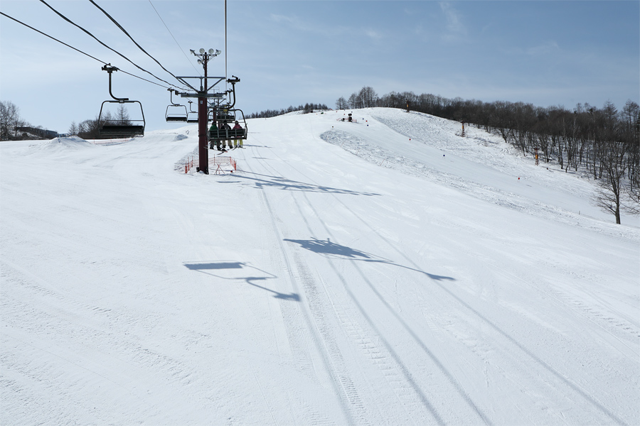 Skiing scene at Shirakabako Royal Hill in Japan, featuring a skier gliding down snowy slopes and a ski lift carrying more sports enthusiasts to the ski resort.