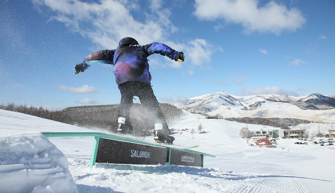 A snowboarder and skier navigating the winter sports scene at Shirakabako Royal Hill Ski Resort in Nagano, Japan, with a ski lift observable in the backdrop.
